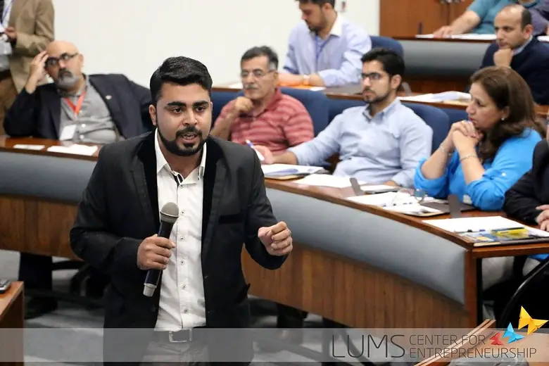 Speaker with a microphone addressing a seated audience in a lecture hall
