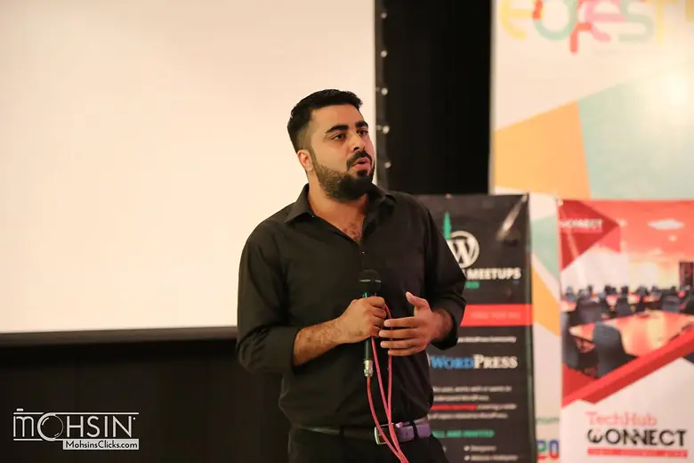 Speaker with a microphone beside WordPress Meetups Pakistan and TechHub Connect banners