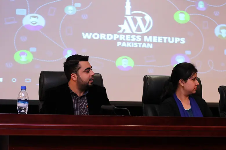 Two panelists seated in front of a WordPress Meetups Pakistan screen